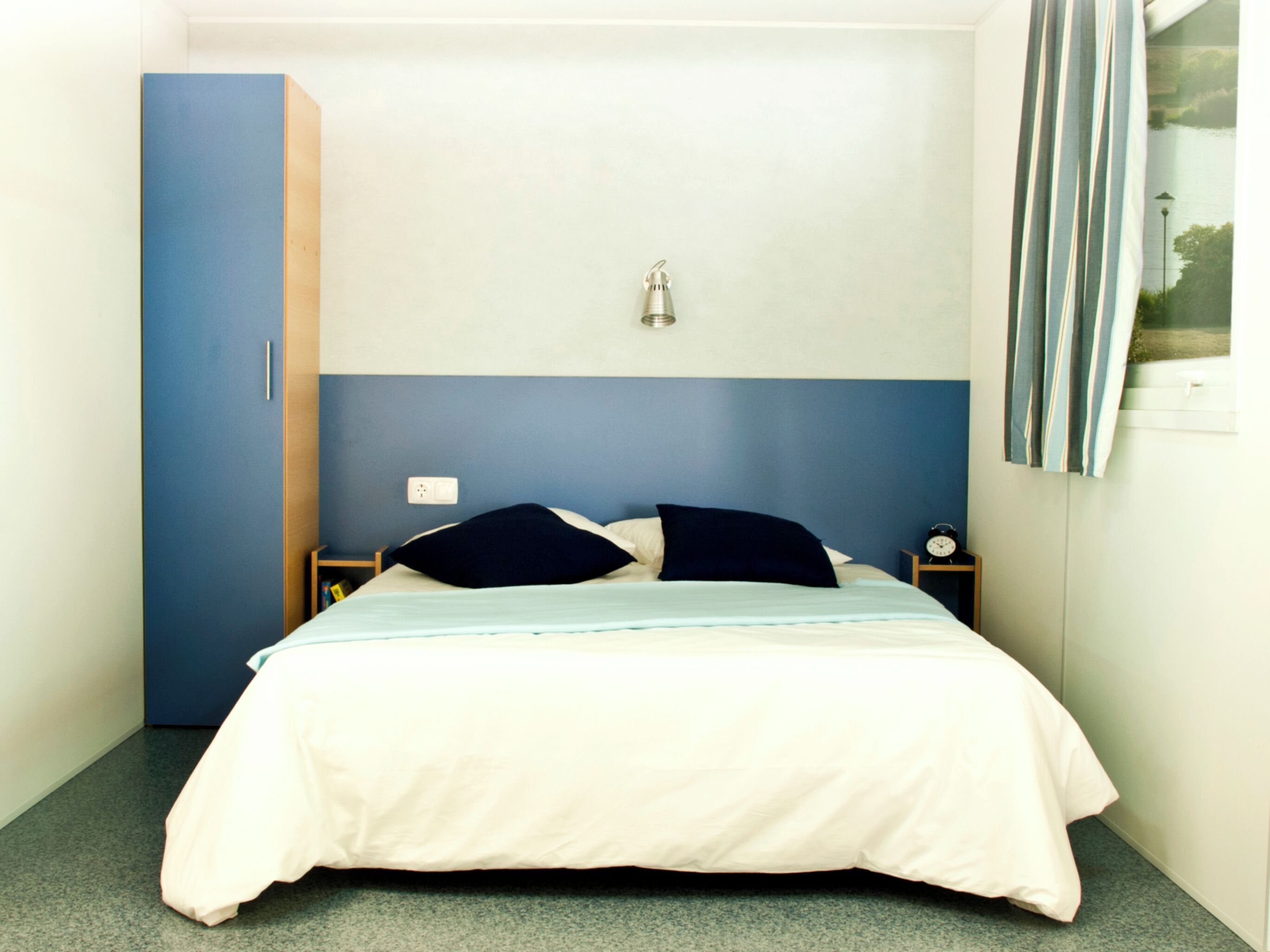 Une chambre à coucher comprenant un lit, une table de chevet, une lampe fixée au mur et une armoire.