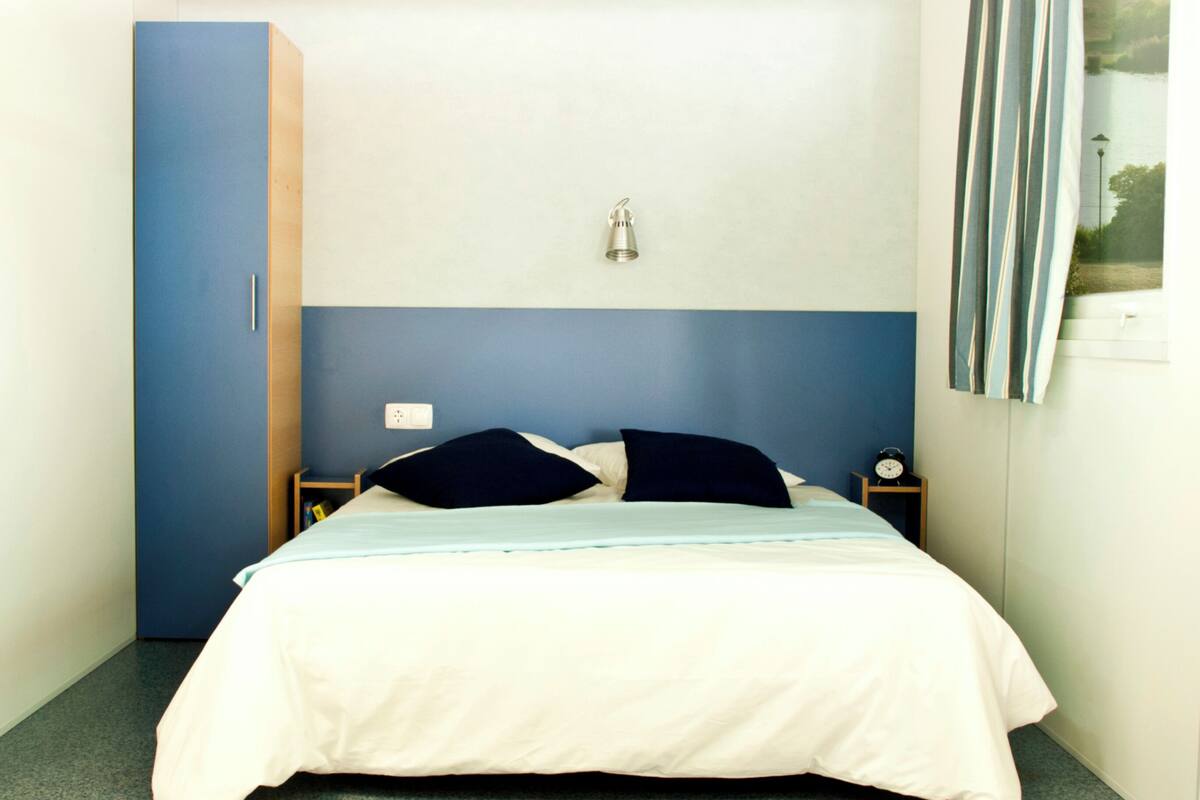 A bedroom with a bed, a nightstand, a wall-mounted lamp, and a wardrobe.