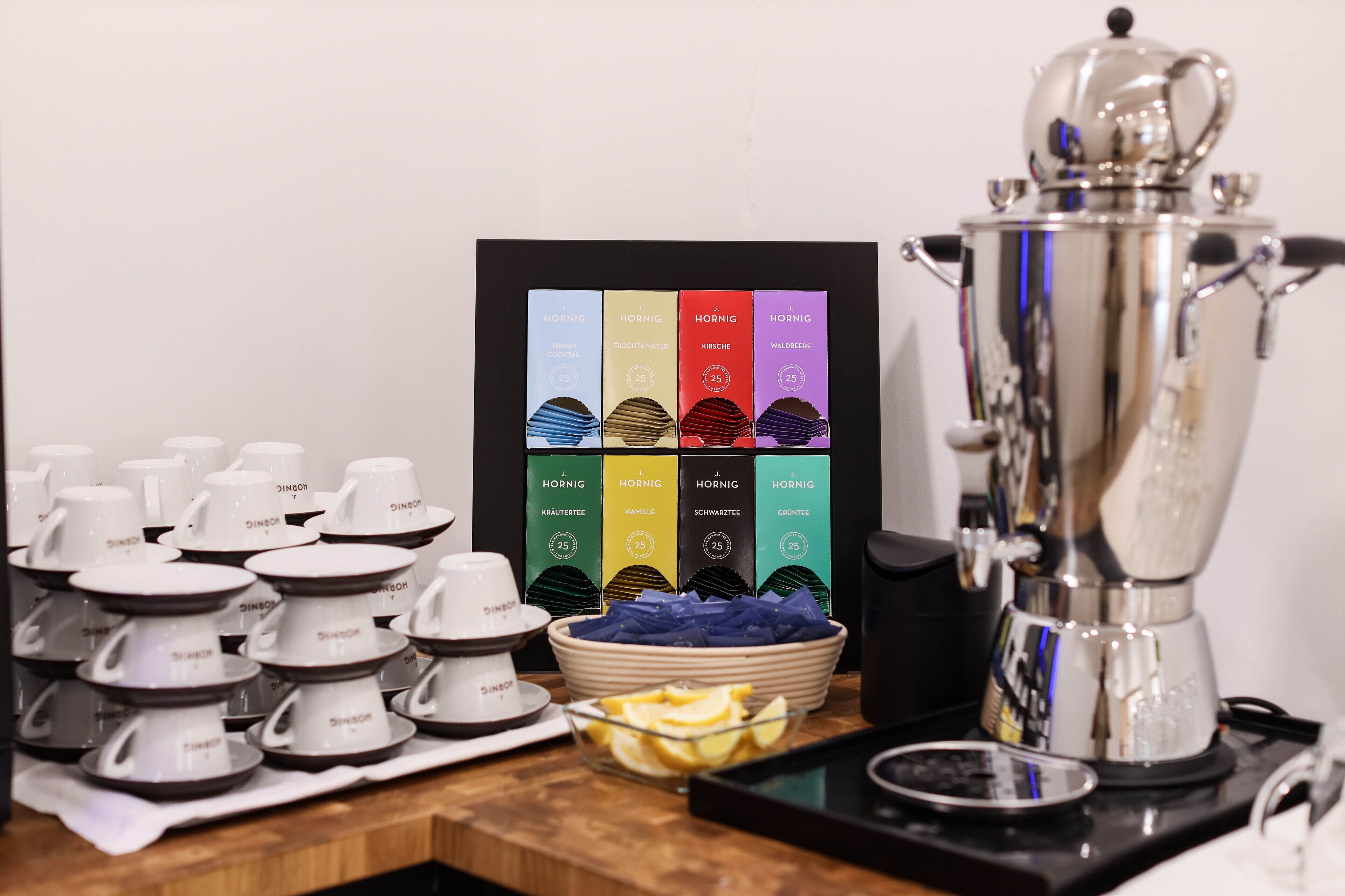 A coffee station with a coffee maker, cups, and a display of coffee flavors.