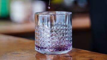 A hand pouring a liquid from a metal jigger into a clear glass with a textured pattern.