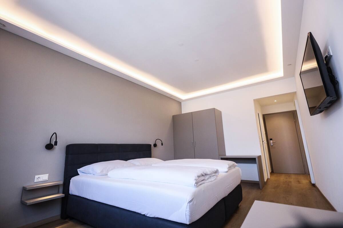 A modern hotel room with a large bed, bedside tables, a wardrobe, and a television mounted on the wall.