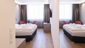 Ein modernes Hotelzimmer mit zwei Betten, einem kleinen Schreibtisch und einem Spiegel, der den Raum widerspiegelt.