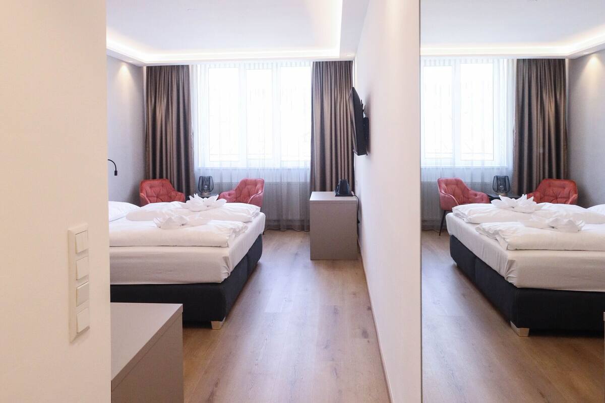 A modern hotel room with two beds, a small desk, and a mirror reflecting the room.
