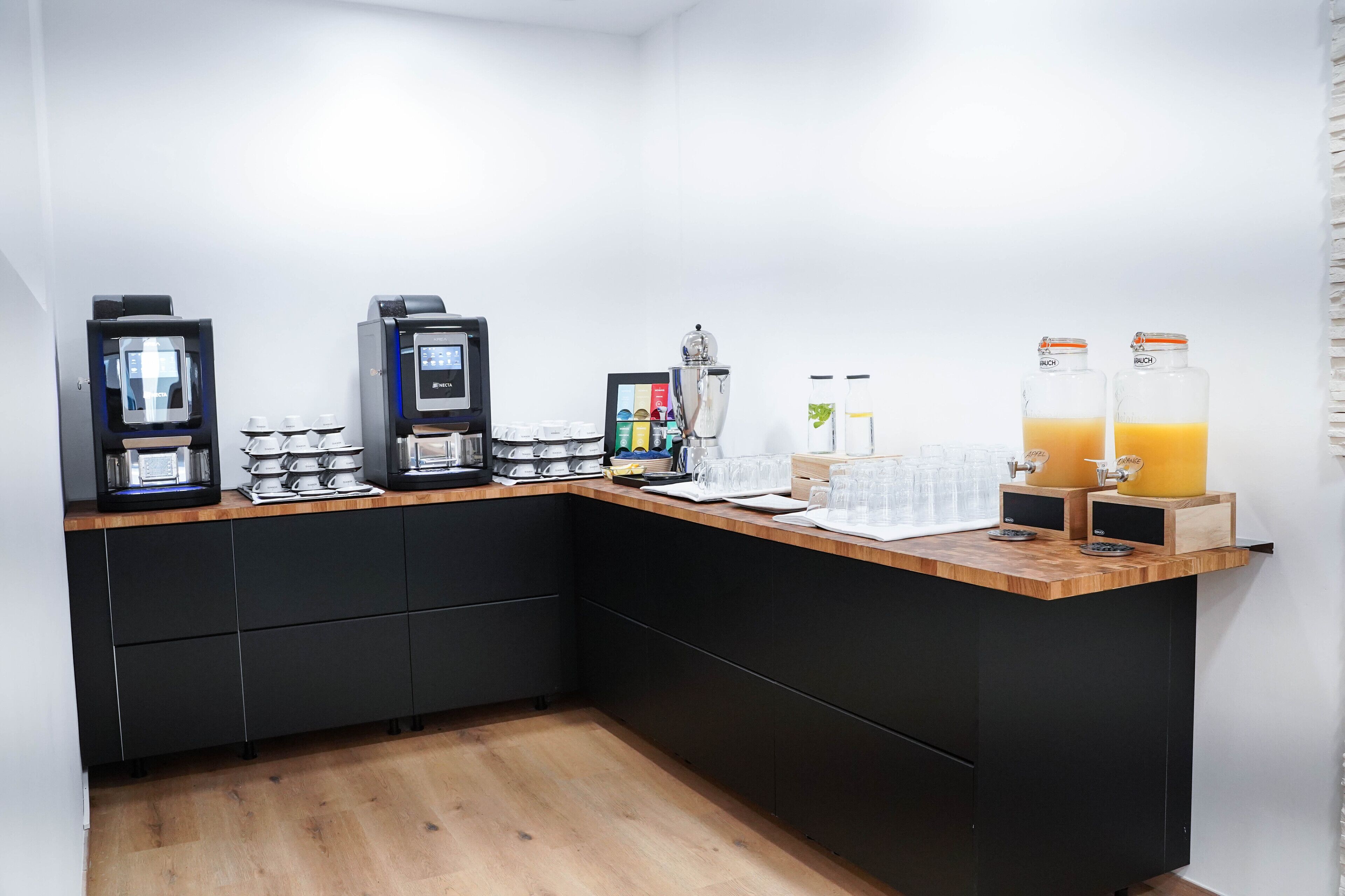 Una cocina moderna con encimera de madera, armarios negros y varios electrodomésticos, incluyendo cafeteras y una licuadora.