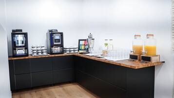 Una cocina moderna con encimera de madera, armarios negros y varios electrodomésticos, incluyendo cafeteras y una licuadora.
