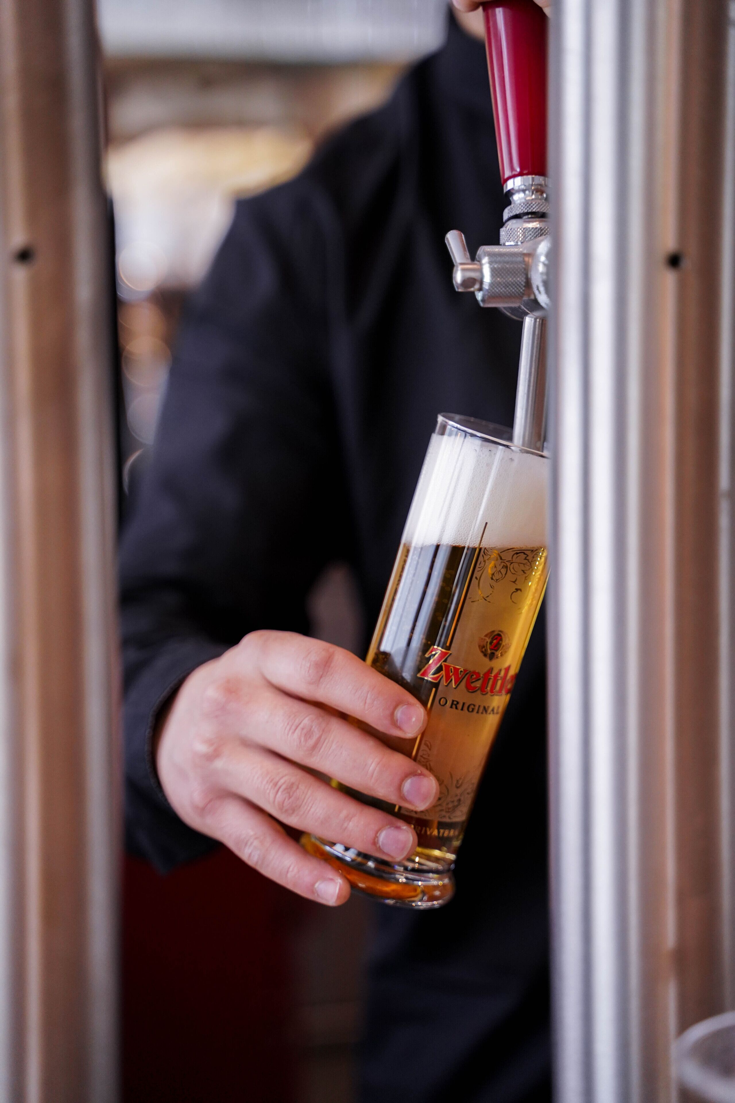 A person holding a glass of beer with a tap above it.