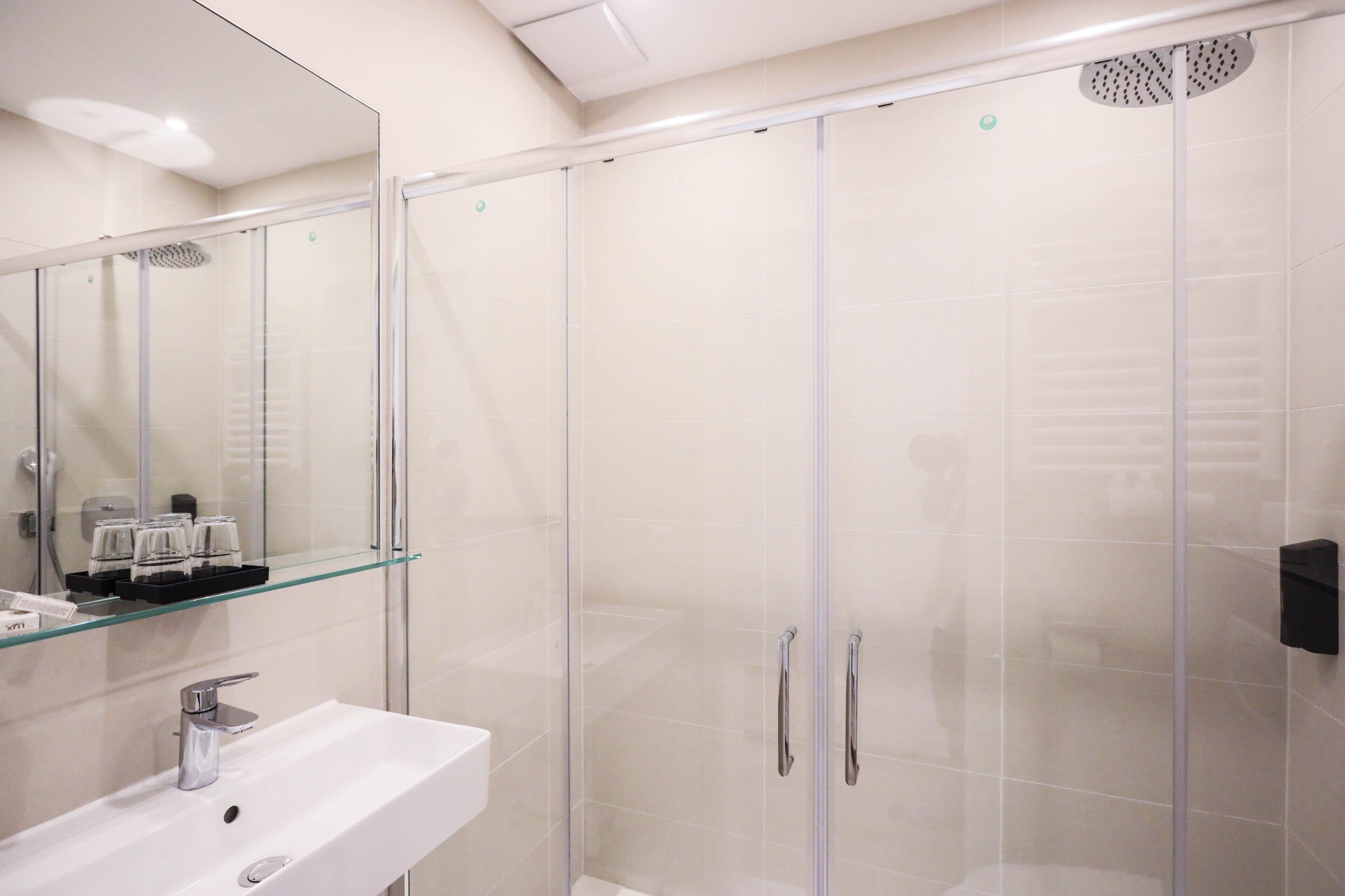 Ein modernes Badezimmer mit einer gläsernen Duschkabine, einem weißen Waschbecken und einem Glasregal für Pflegeprodukte.