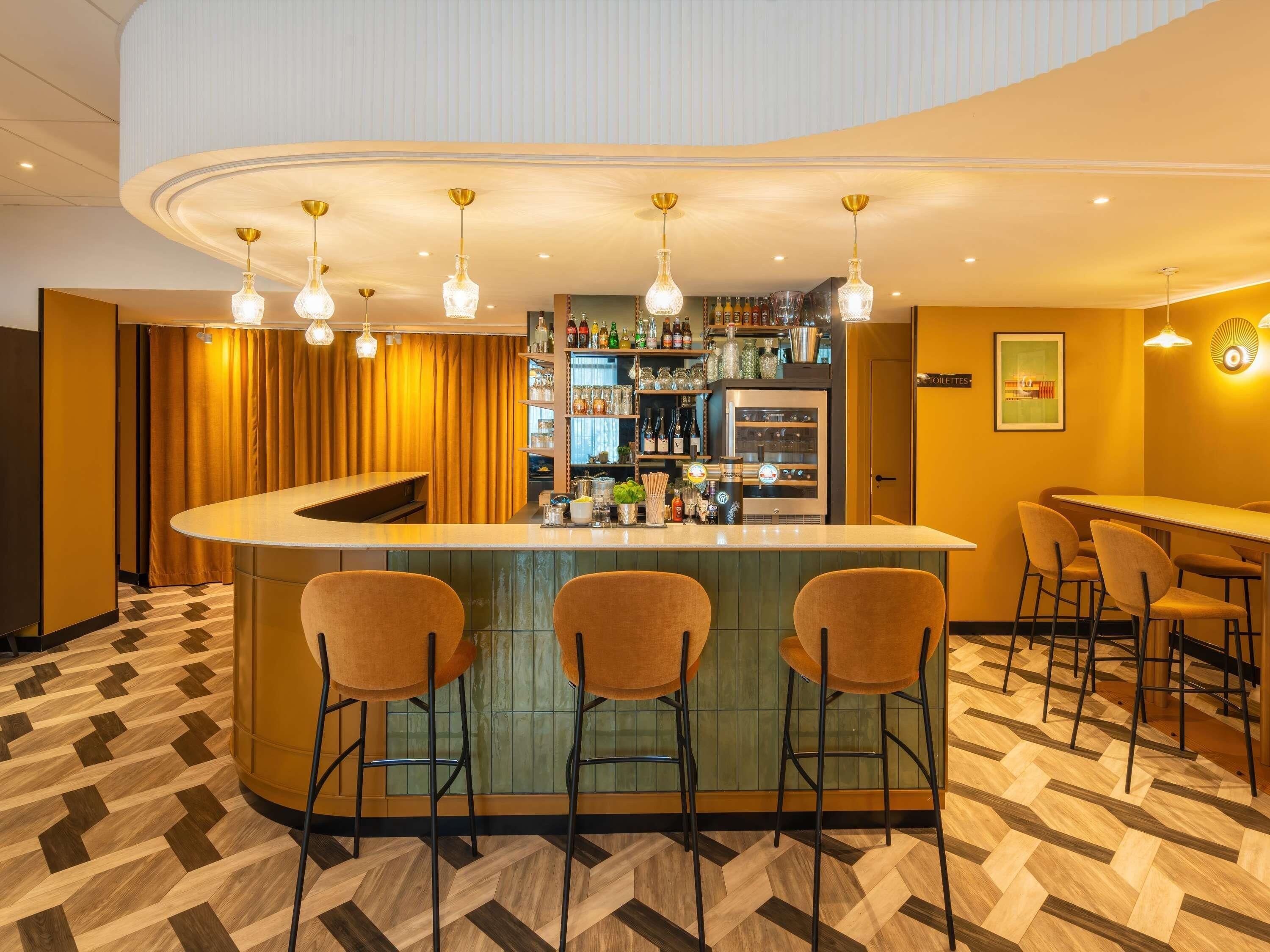 A bar area with a curved counter, bar stools, and hanging pendant lights.