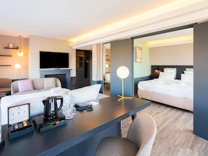 Una habitación de hotel moderna con sofá, escritorio con cafetera, televisor de pantalla plana y cama.