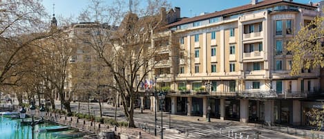 A hotel with a classic European architectural style, a waterfront view, and a pedestrian walkway.