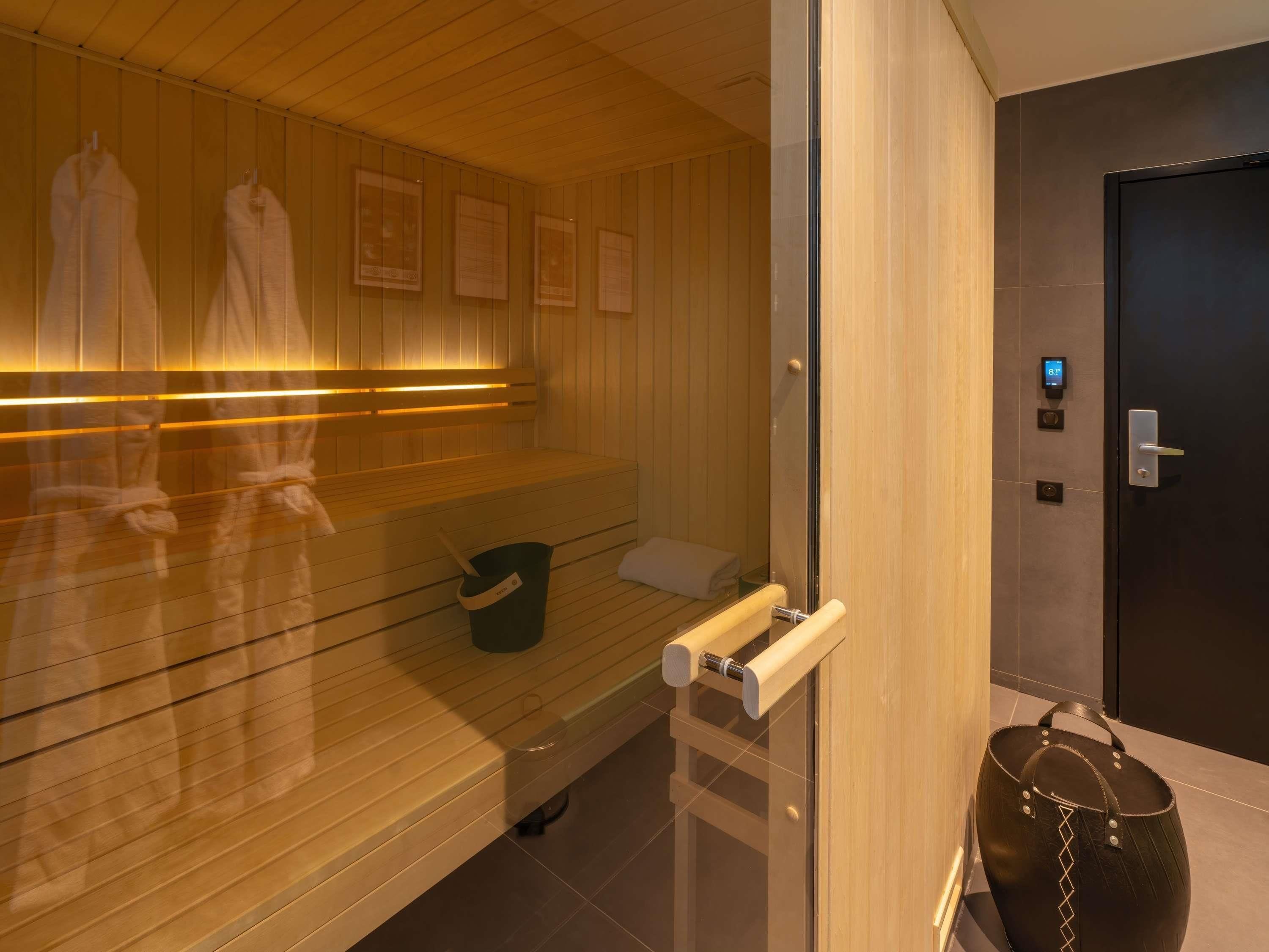 Una sauna con bancos de madera, un perchero para toallas, un cubo y una puerta con pantalla digital.