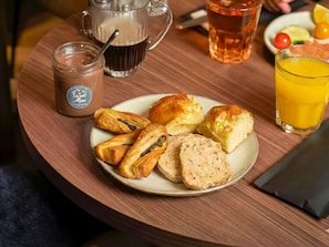 A plate of pastries, a glass of orange juice, a mug of coffee, and a glass of tea on a wooden table.