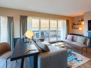 A modern living room with a sofa, a dining table, and a large window with curtains. - Splendid Hotel Lac d'Annecy - Handwritten Collection (Annecy)