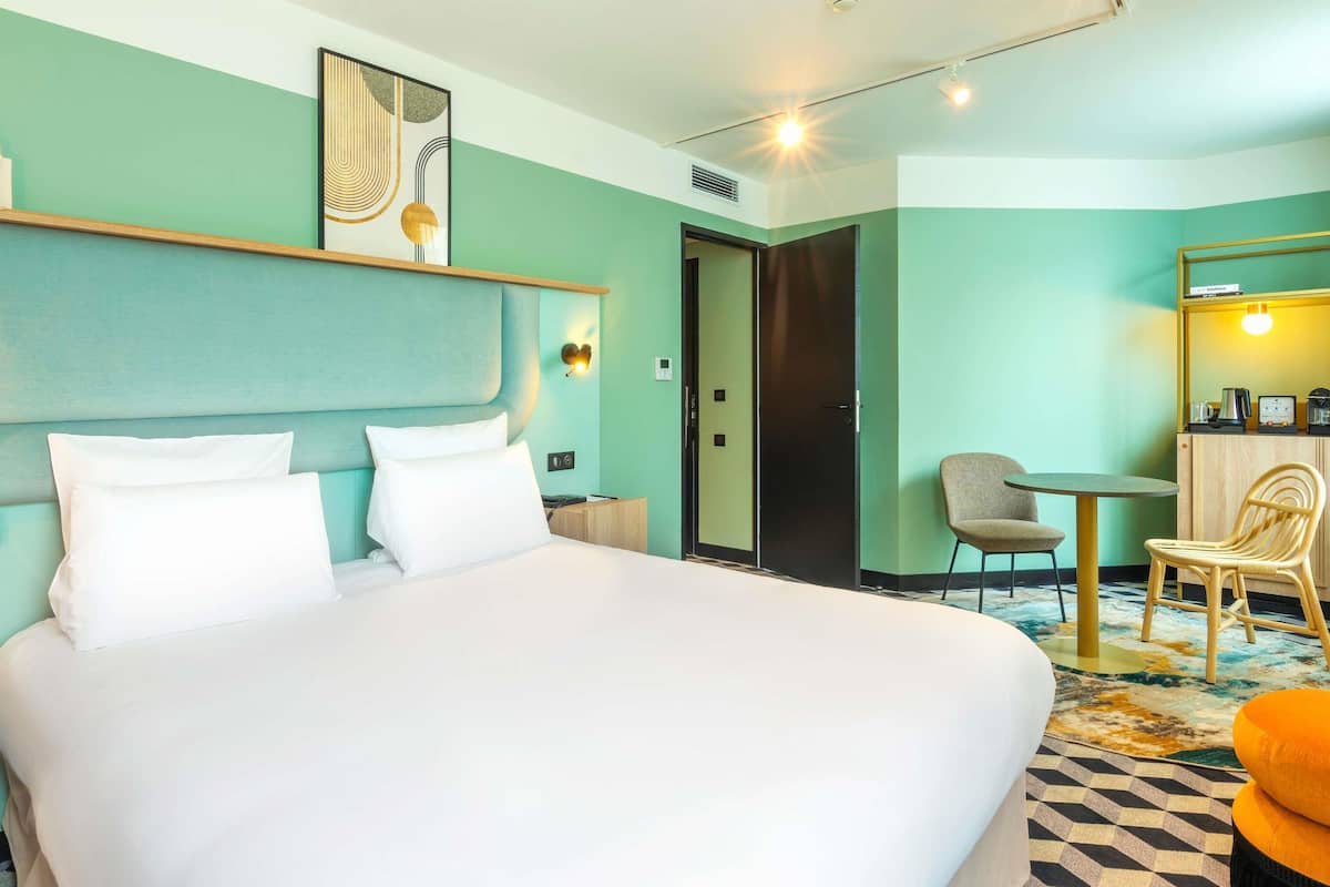 A hotel room with a large bed, a desk with a chair, and a small table with a chair.