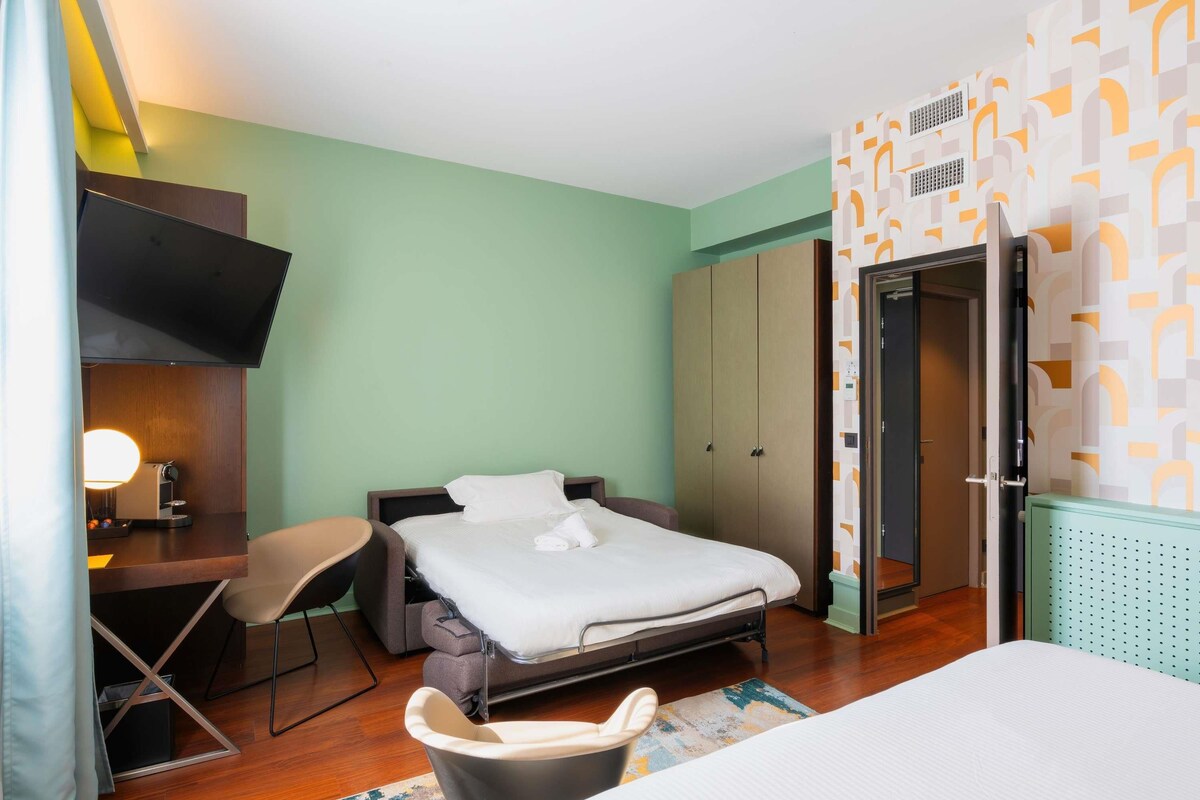 Hotellihuone, jossa on sänky, työpöytä tuolilla, televisio ja vaatekaappi.