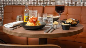 A dining table with a bowl of spaghetti, a bottle of Charles Papillon, glasses, and bread on a restaurant booth. - Splendid Hotel Lac d'Annecy - Handwritten Collection (Annecy)