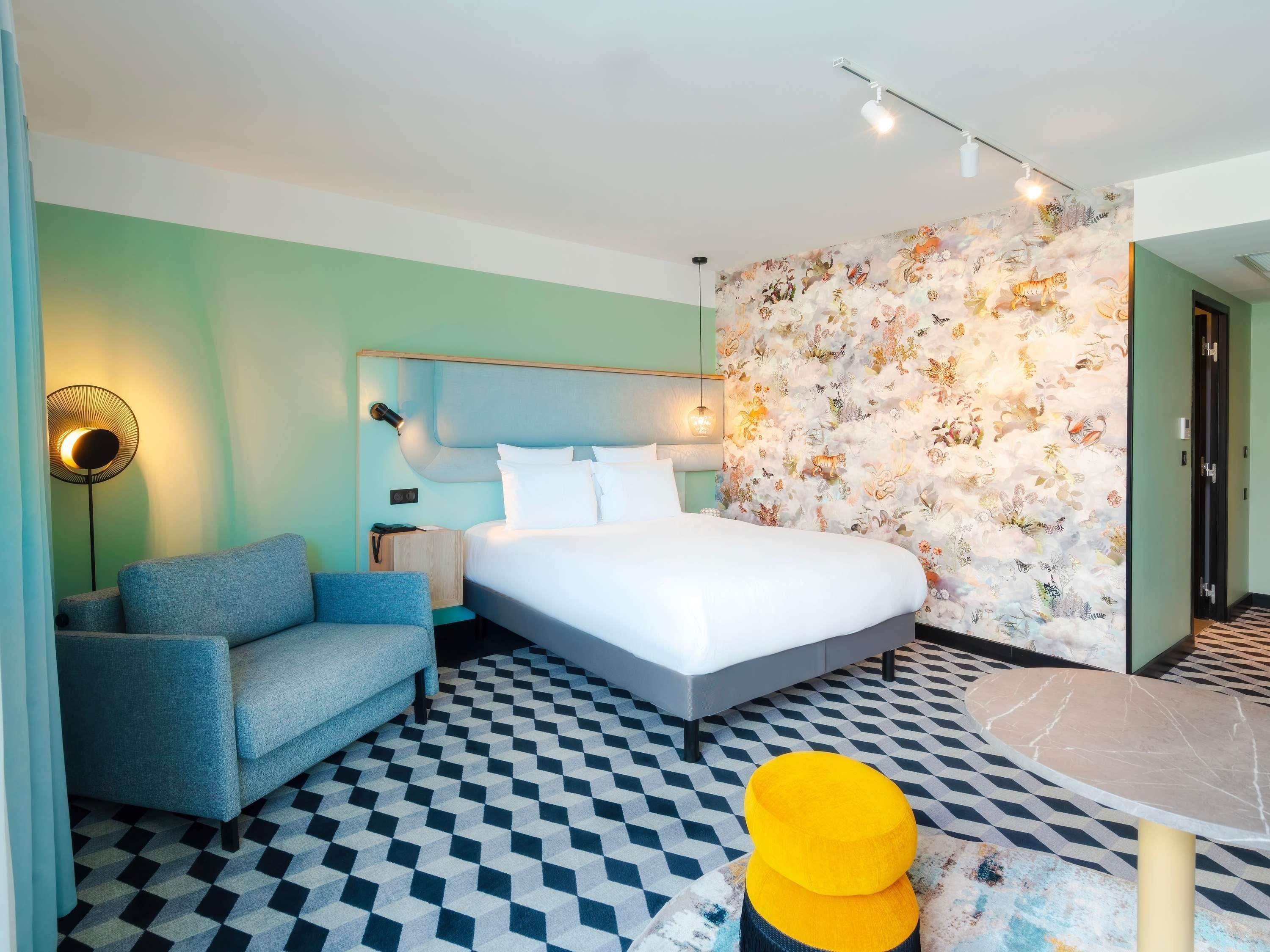 A modern hotel room with a bed, a sofa, a small table, and a patterned floor.