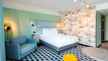 A modern hotel room with a bed, a sofa, a small table, and a patterned floor.