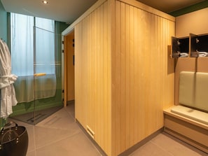 A modern bathroom with a glass shower enclosure, wooden paneling, and a bench with towels.