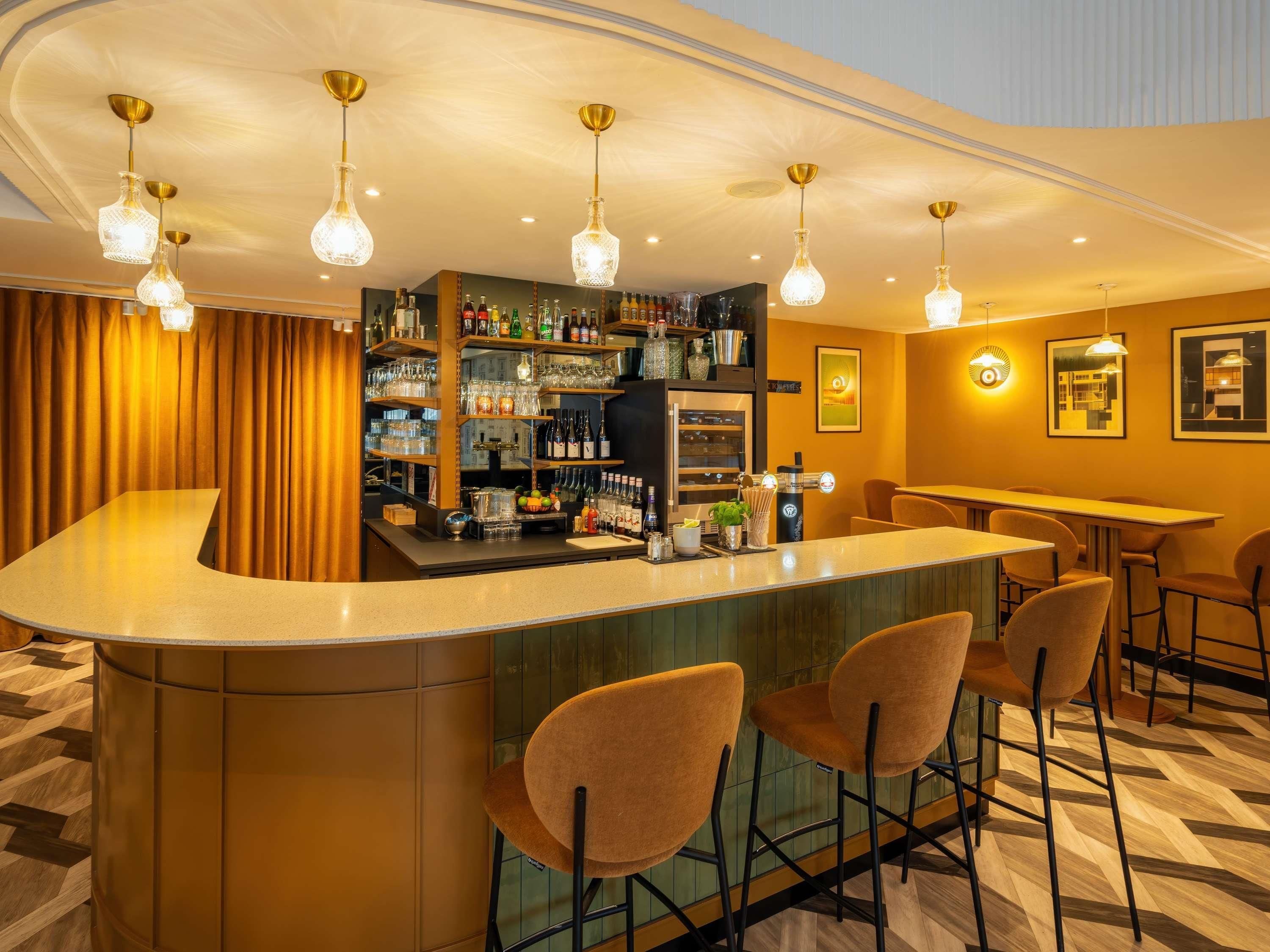 A bar area with a curved counter, bar stools, and hanging light fixtures.