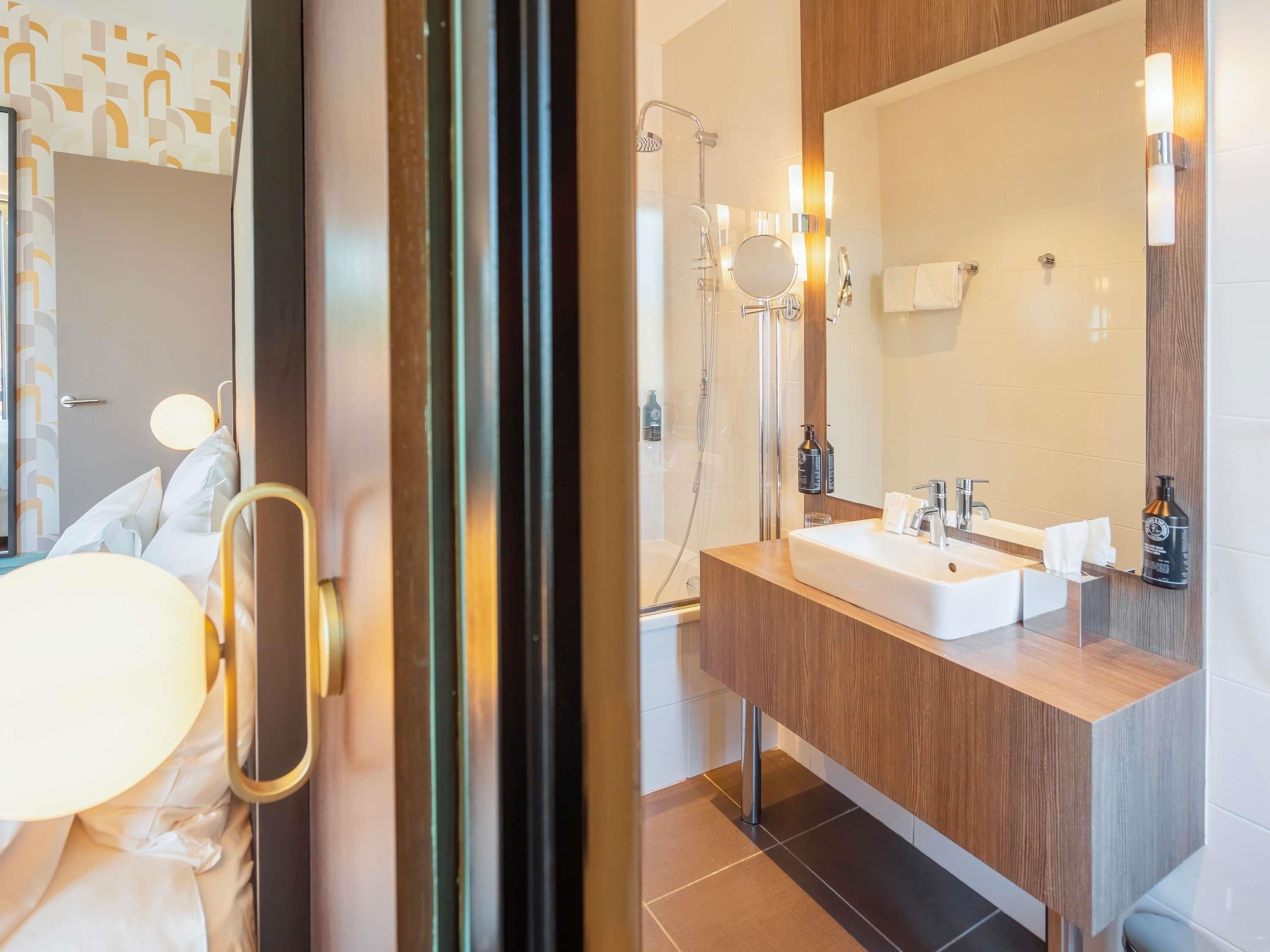 A modern bathroom with a large mirror, a sink, and a shower.