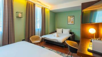 Una habitación de hotel con una cama, dos sillas, un escritorio con lámpara y una ventana con cortinas.