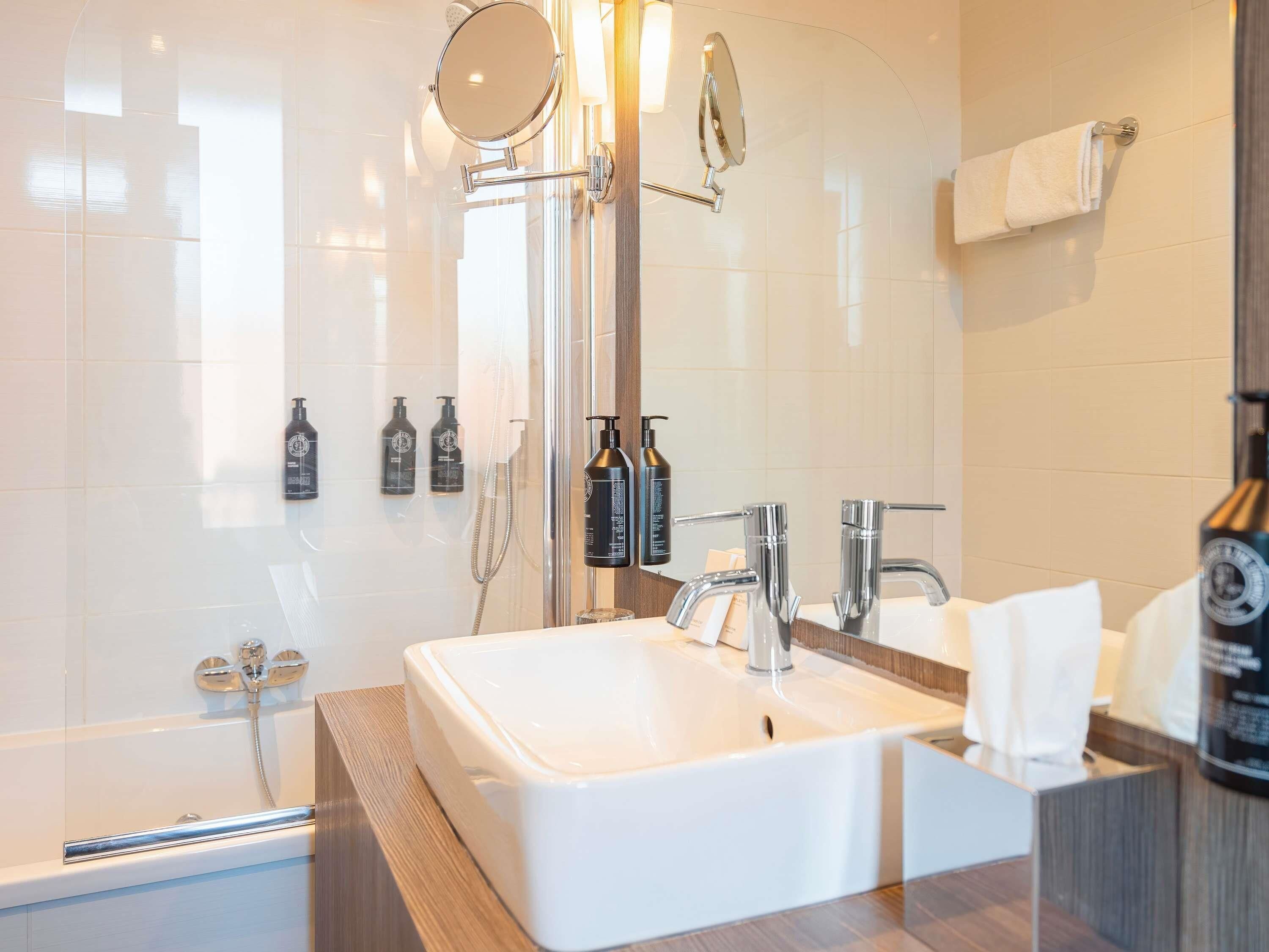 Ein modernes Badezimmer mit einem großen Waschbecken, einem Spiegel, einer Dusche und zwei Shampoo-Flaschen.