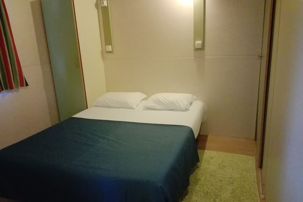 Une petite chambre avec un lit simple, une couvre-lit verte, des oreillers blancs et un tapis vert.