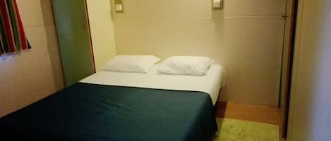 A small, single-bed room with a green bedspread, white pillows, and a green rug.