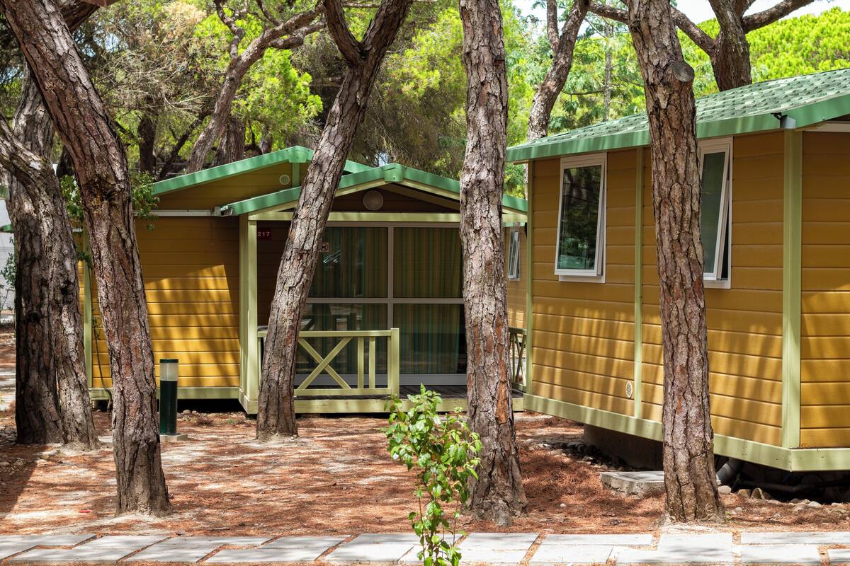 Una fila de cabañas amarillas con techos verdes, rodeadas de árboles.