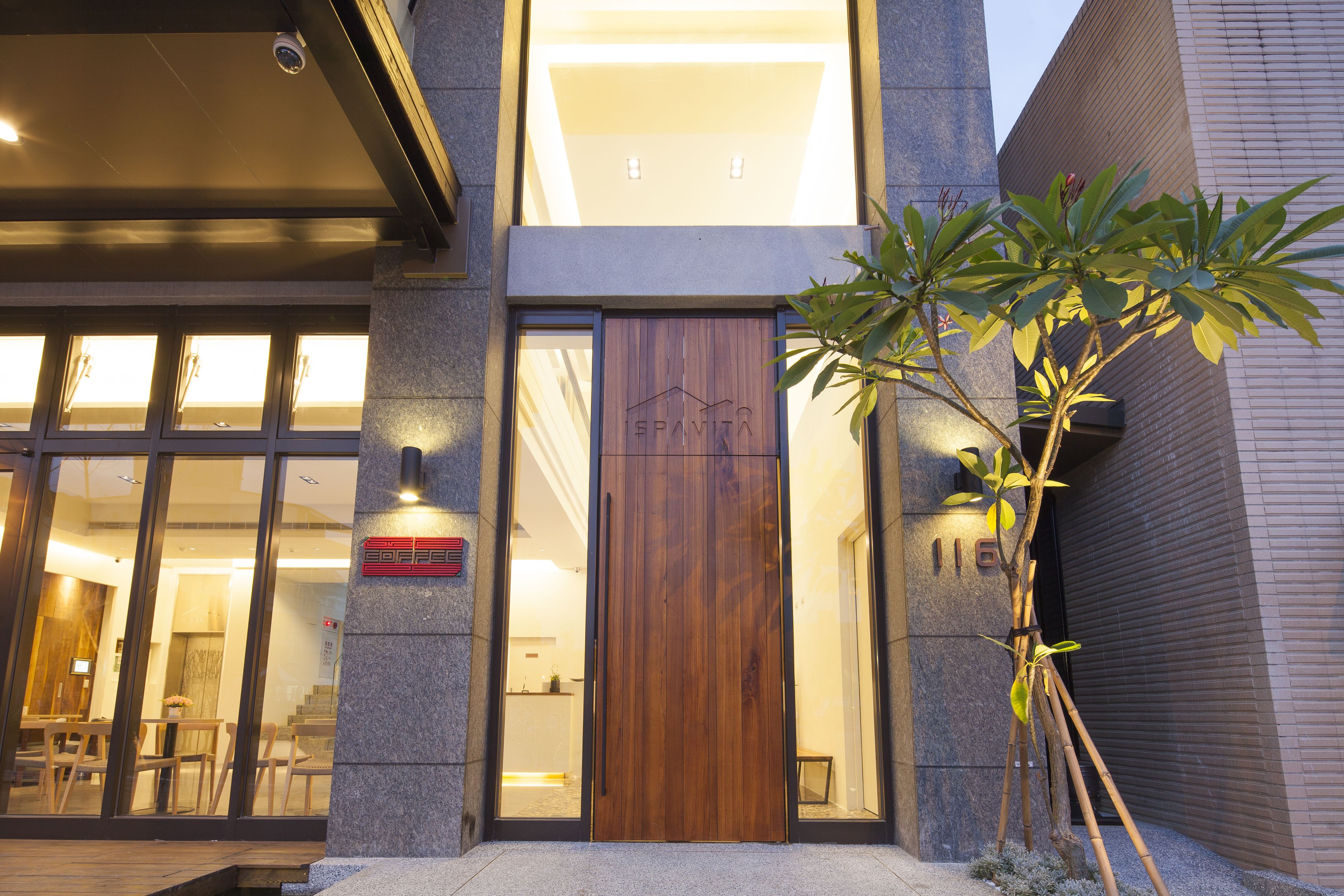 A modern building with a wooden door, large windows, and a small tree in front.