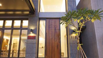 A modern building with a wooden door, large windows, and a small tree in front.