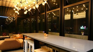 Un espace bar moderne avec un long comptoir, des tabourets et un luminaire suspendu au plafond.