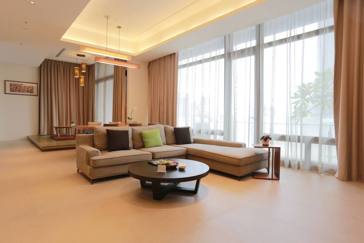 Un salón moderno con un sofá modular, una mesa de centro redonda y ventanas amplias con cortinas.