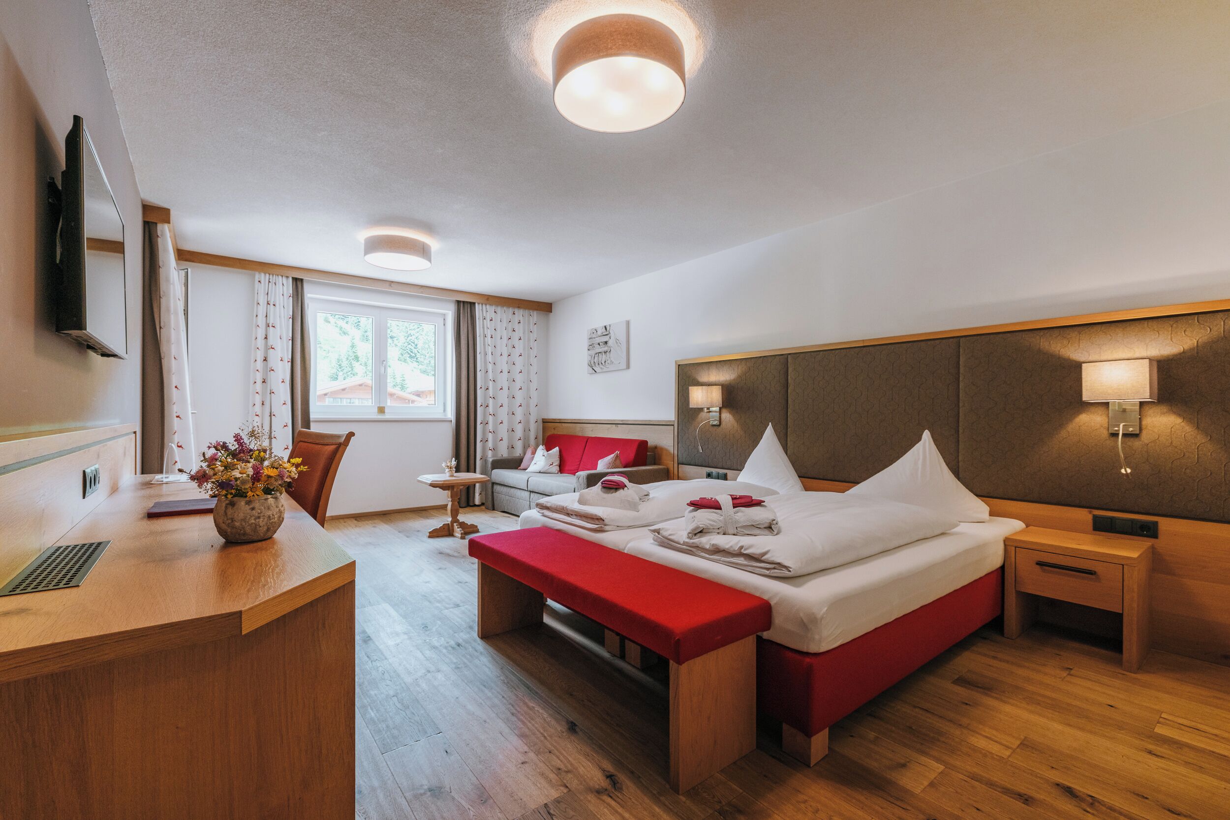 Habitación de hotel con cama, mesitas de noche, escritorio, silla, ventana y televisor montado en la pared.