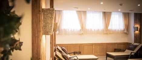 A room with wooden paneling, a large window with curtains, and a seating area with lounge chairs and a small table.