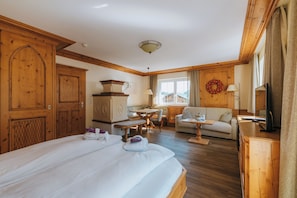A hotel room with a large bed, wooden furniture, a dining area, and a view of the outside. - Anthonys Alpin Hotel (Lech am Arlberg)