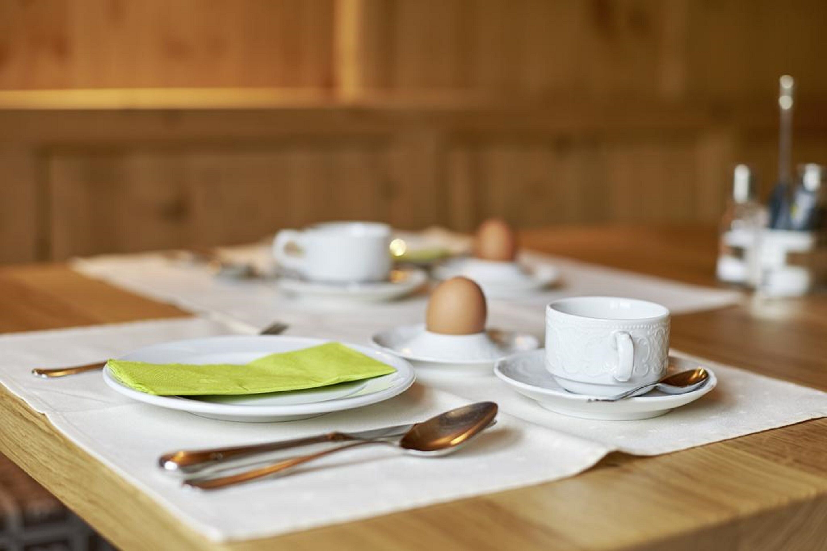 Une table en bois mise pour le petit-déjeuner, avec des assiettes, des tasses et des couverts.