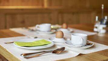 Ein gedeckter Frühstückstisch mit Tellern, Tassen und Besteck auf einer Holztischplatte.