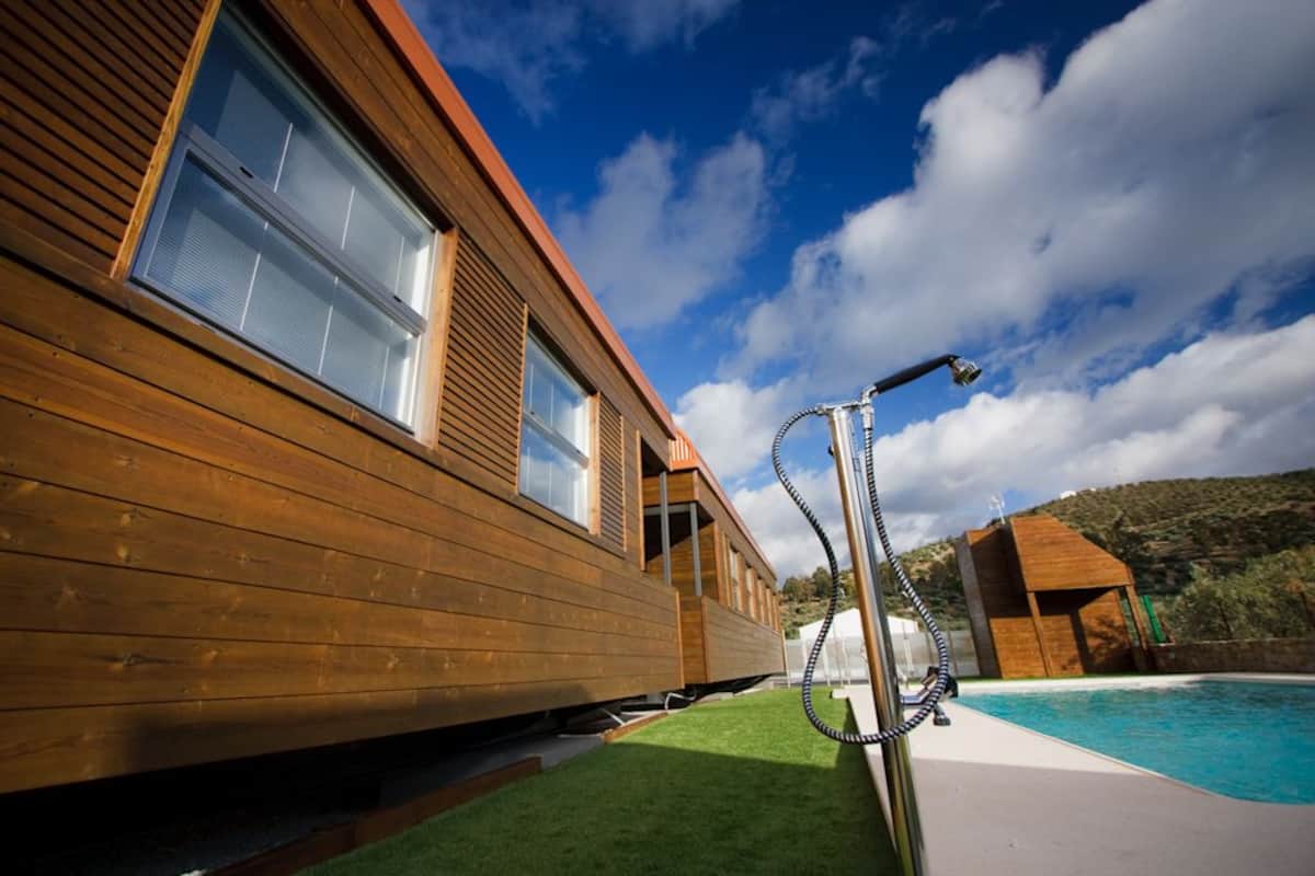 Una casa moderna de madera con un amplio ventanal y una piscina al fondo.