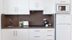 A compact kitchen with white cabinets, a sink, a microwave, and a refrigerator. - Casa Vagón Vía Verde Sierra (Olvera)