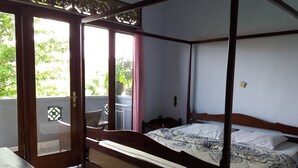 A four-poster bed with a floral bedspread, a wooden headboard, and a view of greenery outside. - Celagi Inn (Padangbai)