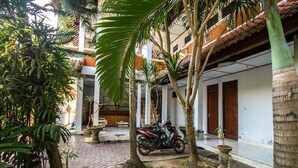 A courtyard with a paved walkway, palm trees, and a parked motorcycle. - Celagi Inn (Padangbai)