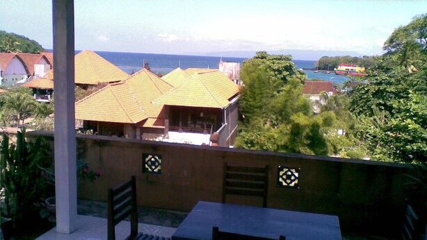 A balcony with a table and chairs, overlooking a coastal area with houses and a boat. - Celagi Inn (Padangbai)