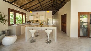 Una cocina moderna con una isla central, taburetes blancos y un amplio ventanal.