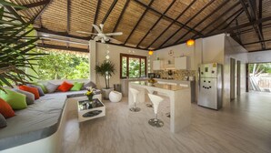Una cocina moderna con una isla central, un comedor con taburetes de bar, un sofá con cojines coloridos y un ventilador de techo.