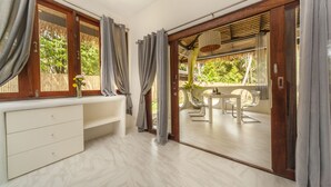 Una habitación con baño, un comedor con mesa y sillas, y vista a un jardín a través de una puerta de vidrio.