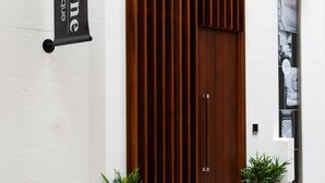 Una entrada moderna con una puerta de madera grande, un letrero que dice “welldone” y plantas en macetas a ambos lados.