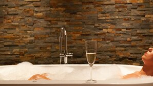 Una bañera con una copa de champán, una pared de piedra y un grifo.
