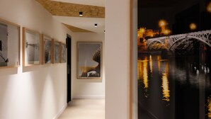 Un pasillo con obras de arte enmarcadas en las paredes, un ventanal con vistas a un puente y al agua, y piso alfombrado.